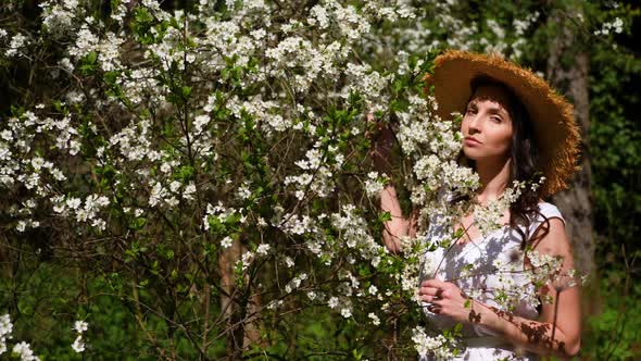 Brunette Woman with Long Hair in a Straw Hat Stands in the Apple Orchard