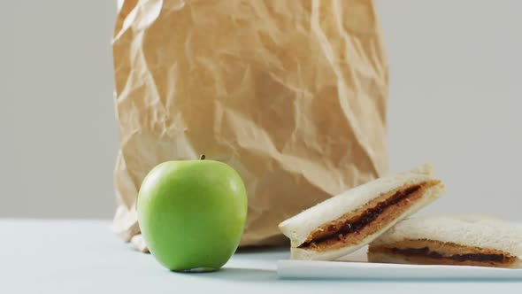 Peanut butter and jelly sandwich with apple and paper bag against white background