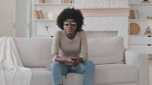 Happy Young African American Woman Wearing 3d Glasses Sitting on Cozy Couch Switching Channels Using
