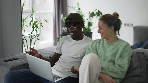 Happy Biracial Couple Sitting on Sofa with Laptop Congratulating Each Other