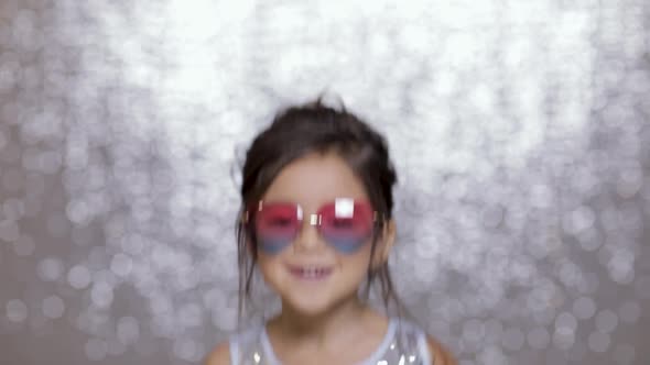 Cute Happy Little Girl Child in a Silver Dress Dancing on Background of Silver Bokeh