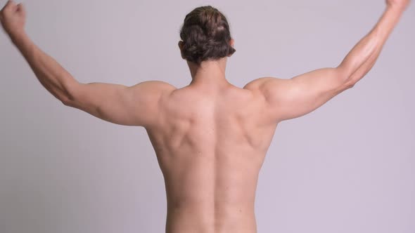 Rear View of Muscular Man Flexing Biceps Shirtless Against White Background