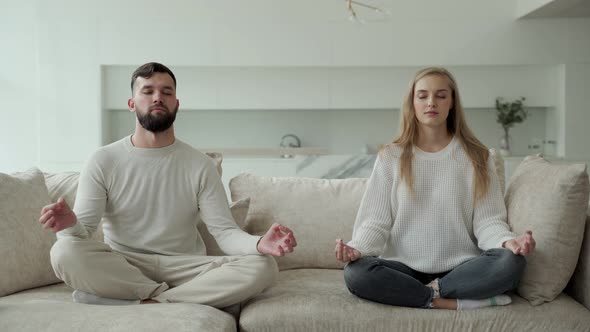 Calm Young Family is Doing Yoga Together Sitting in the Lotus Position on the Sofa