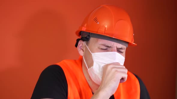 Male Construction Worker in Overalls and Medical Mask Coughing on Orange Background