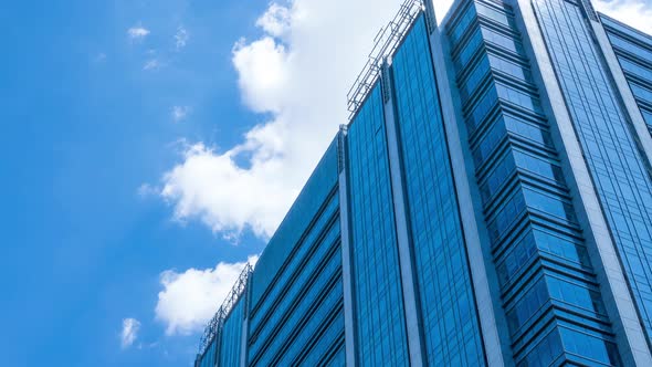 Time lapse, looking up at a glass-covered skyscraper, reflecting the blue sky and passing clouds