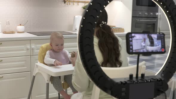 Recording Video with Mobile Phone and Ring Light of Mother Feeding Her Oneyearold Baby Boy with