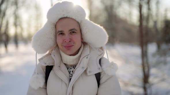 Young Man with Traditional Russian Fur Ushankahat is Walking in Park in Winter Day