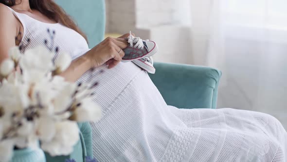 Small Shoes for the Unborn Baby on the Belly of Pregnant Woman