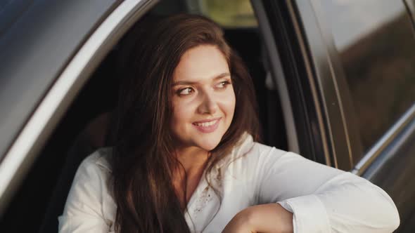 Pretty Girl Leans Out Car Window Looks Outside and Smiles at Camera