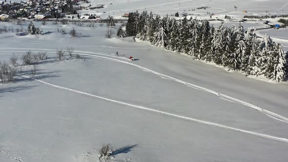 Drone aerial view of winter fun on snow, snowmobile towing skier on flat ground on sunny day