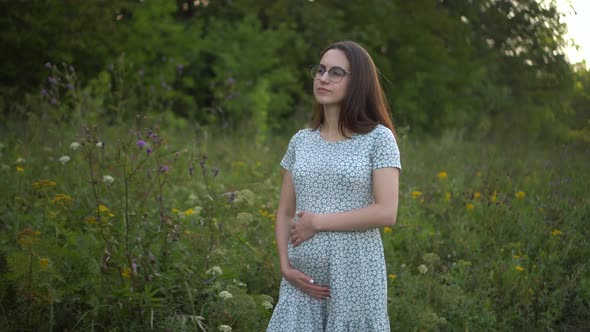 Happy Young Pregnant Woman Walks in Nature and Strokes Her Belly