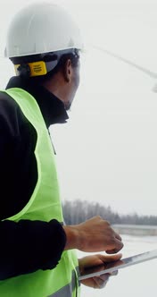 A Man in a Work Uniform is Diagnosing a Wind Turbine Using a Digital Tablet