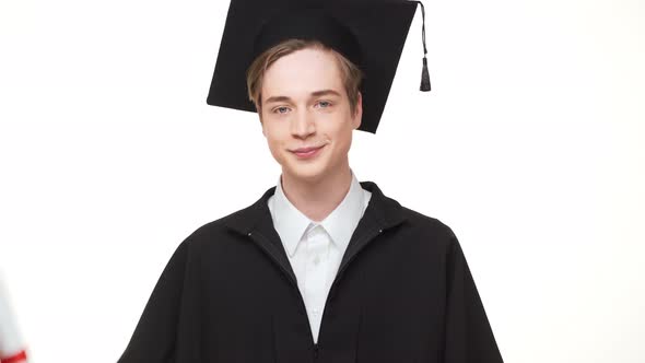 Caucasian Young Male in Black Square Academic Cap and Robe Holding Scroll and Showing Ok on White