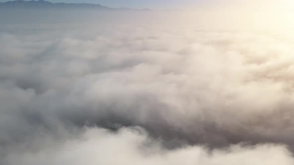 Aerial shot of flying over a layer of soft clouds at dawn