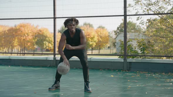 Black Man Dribbling Basketball on Court in the Park and Looks at the Camera