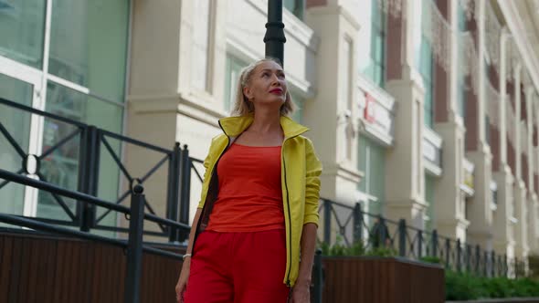 a Blonde in Red Clothes and a Yellow Jacket Leaned Against a Pole on a City Street