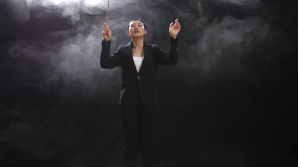 Asian Conductor Woman Holding A Baton And Showing Gesture Quickly In The Black Studio With Fog