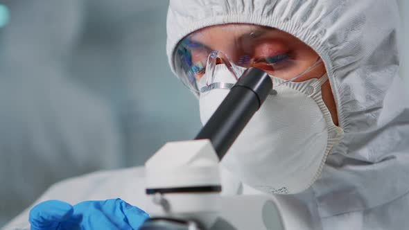 Lab Technician with Protection Suit Examining Samples Using Microscope