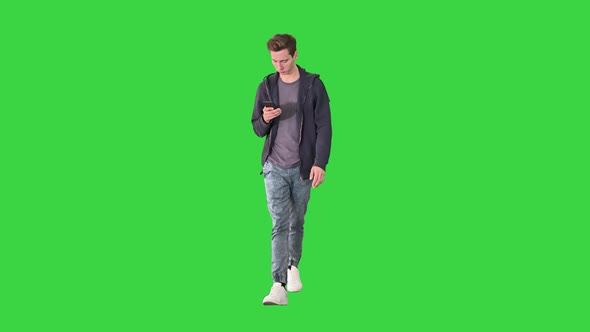 Young Man in Casual Clothes Text Messaging on Cell Phone and Walking on a Green Screen, Chroma Key.