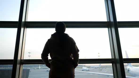 Silhouette of Person Looking Out of Window at Airplanes