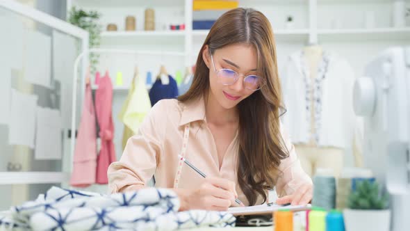 Asian tailor woman design drawing and sketching out ideas for new fashion in tailoring atelier.