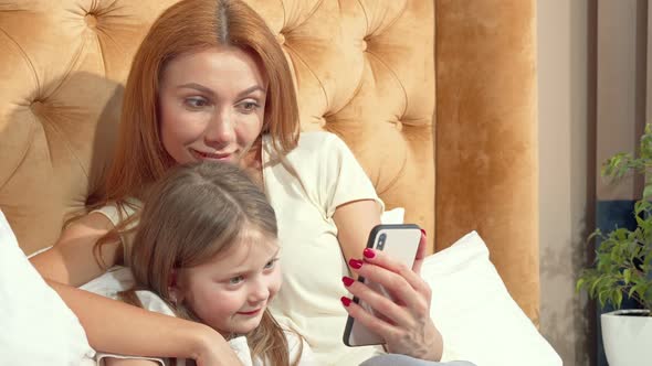 Beautiful Woman and Her Cute Little Daughter Using Smart Phone at Home Together