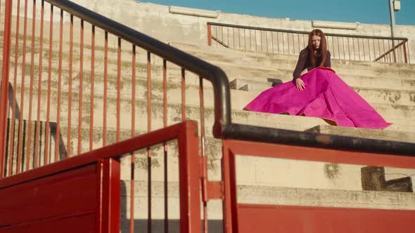 Female Toreo Model With Muleta Seats On Empty Bench In Bullring Arena. Wide Shot