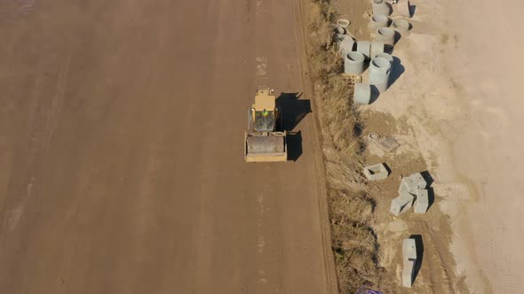 Aerial following shot of a Bulldozer roller compacting dirt in a field next to drain pipes