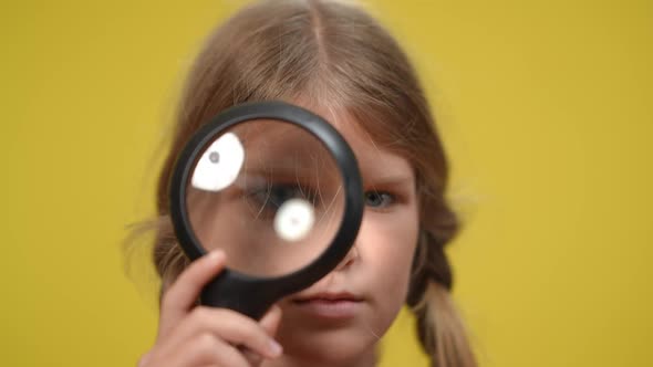 Closeup Face of Teenage Girl with Eye in Magnifier at Yellow Background