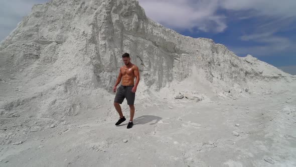 Strong man with athletic body comes to barbell on beautiful white mountain.