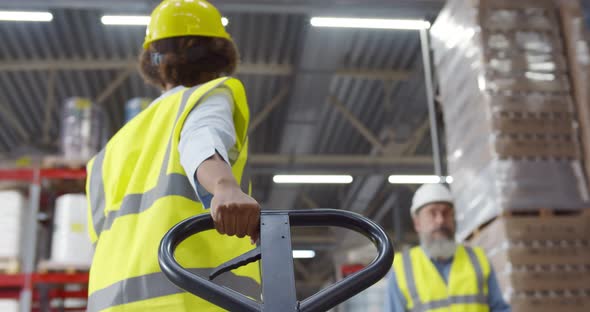 Back View of African Female Warehouse Worker Using Hand Pallet Truck