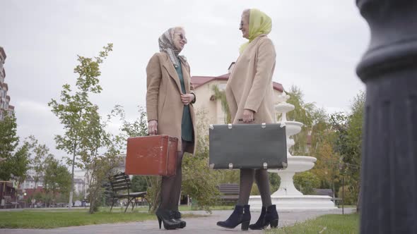 Side View of Mature Caucasian Women in Elegant Clothes and Sunglasses Standing with Travel Bags