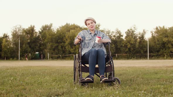 Disabled Woman on Wheelchair with Mug of Coffee in Park Talks About the Difficulties That She Had to