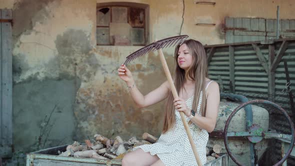 Young Woman Touches Rake Sitting on Old Cart with Firewood