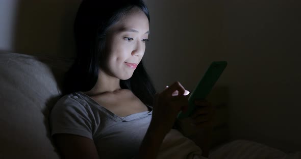 Woman use of mobile phone on bed at night 