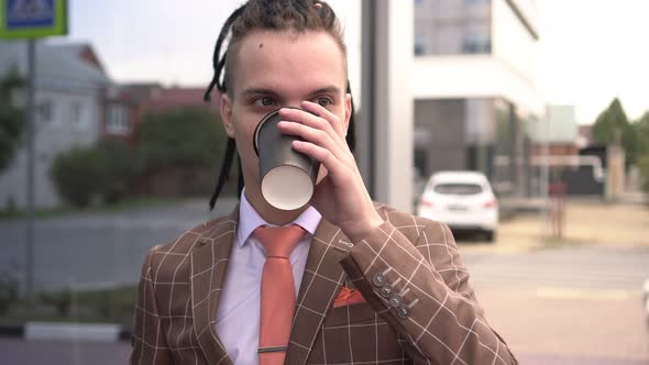 Young Modern Businessman or Manager Drinks Coffee From a Paper Cup Outdoors