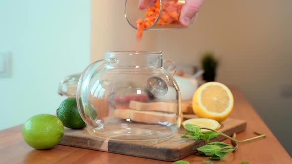 A Man's Hand Pours Frozen Sea Buckthorn Berries From a Glass Into a Teapot