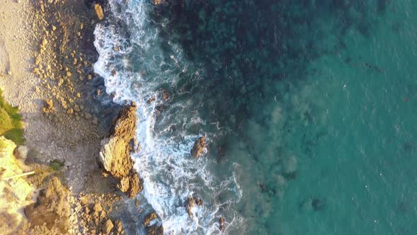 4k ariel drone shot of crystal clear blue waters along the coast of a gorgeous sunny beach.