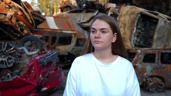Portrait of Young Woman Standing at Car Dump Looking Around with Devastated Facial Expression