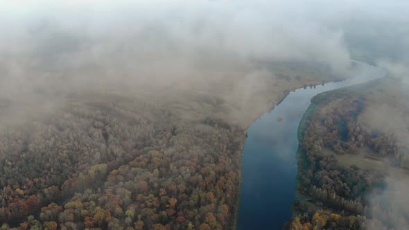 Flying Through a Haze of Clouds To a Stunning Autumn Landscape with a Winding River in the Forest