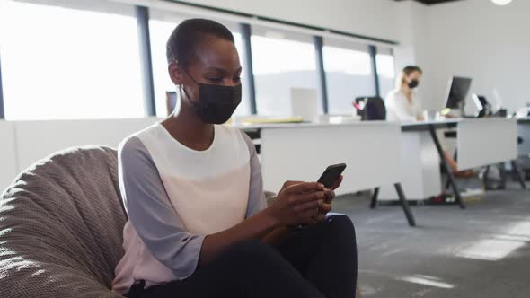 African american businesswoman wearing face mask and using smartphone in office