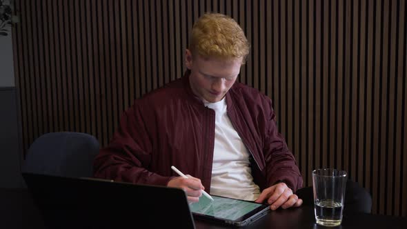 red-haired worker on a remote zoom call taking notes in his office