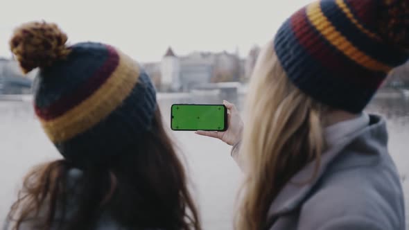 Rear Portrait of Two Young Girlfriends with Smartphone Green Screen in Hands