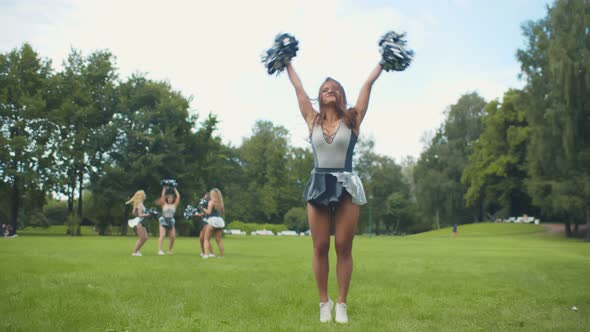 Portrait of Cheerleader in Uniform Jumping in Air with Pompons Practicing Before Performance.