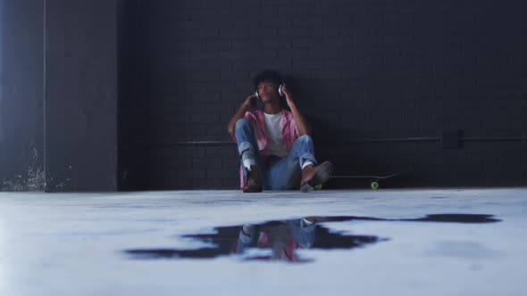 African american man wearing headphones listening to music while sitting in empty parking garage