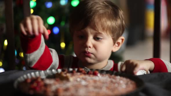 Little kid eating cake at table in fairy lights on background