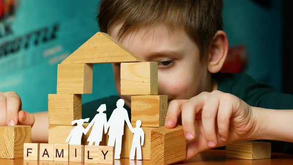 A caucasian boy of 7 years old builds a toy house from wooden cubes, the inscription family alt