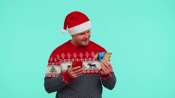 Man in Christmas Sweater Using Credit Bank Card Smartphone While Transferring Money Shopping Online