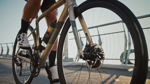 Unknown Young Woman Professional Cyclist in Cycling Shoes and Sportswear is Riding a Bike Along