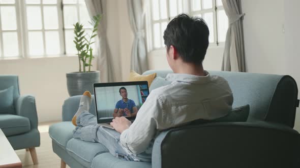 Man Greeting With Colleagues In Video Conference From Laptop At Home Living Room